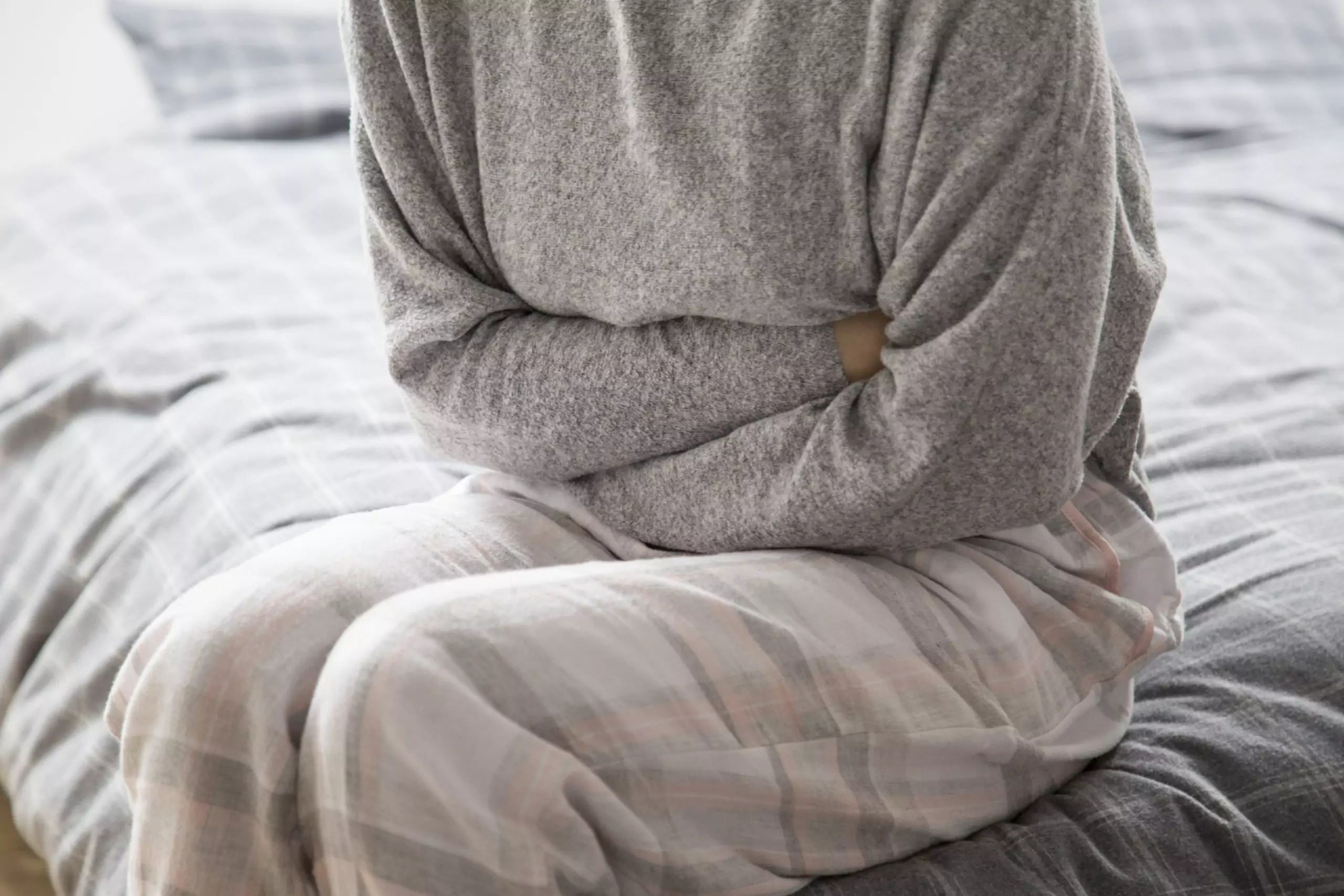 Woman in pajamas sitting on bed holding stomach in pain