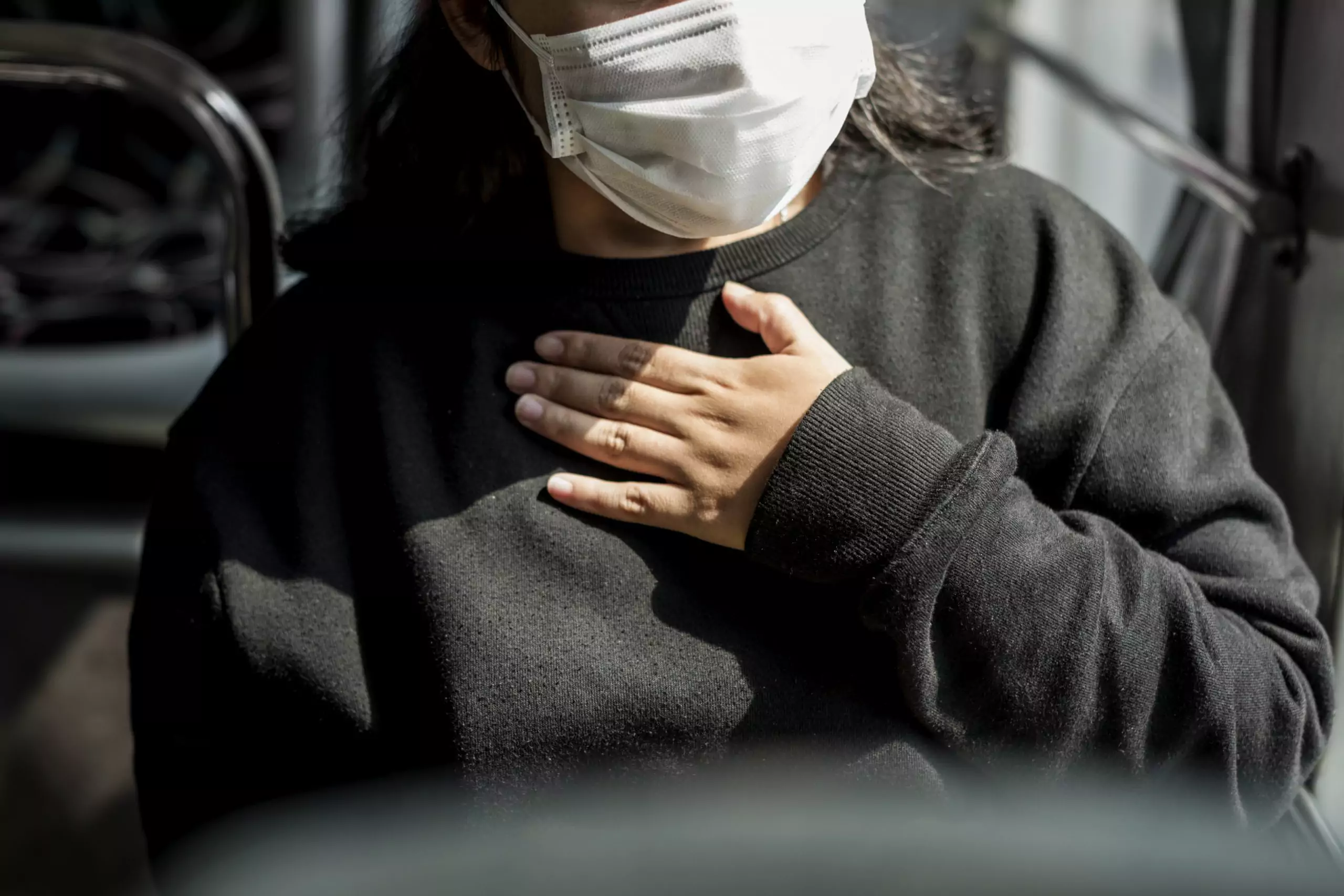 Woman wearing mask on bus with hand on chest trouble breathing long COVID