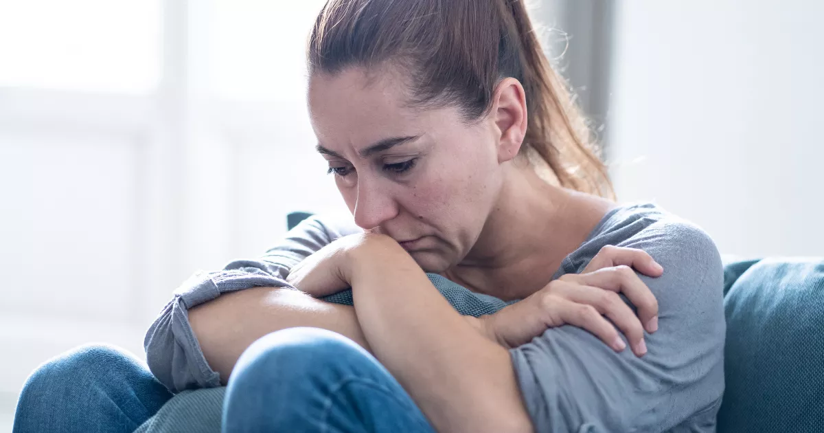 Image of a woman feeling sad, looking down, hugging herself