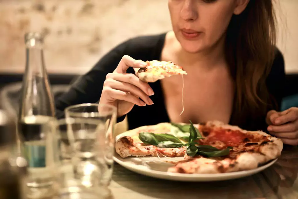 Mujer comiendo pizza como alimento reconfortante para los síntomas de los fibromas